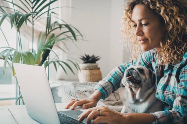 Evde dişi ve yavrusuyla çalışmak akıllıcaydı. Bilgisayarda birlikte çalışmak, dostluk ve sevgi. Neşeli, mutlu kadın dizüstü bilgisayarda bacaklarında bir köpekle yazıyor. Evcil hayvan yaşam tarzı kavramı