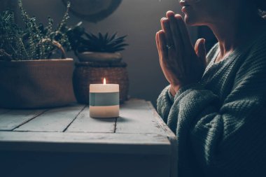 İç yaşam dengesi ve meditasyon kavramı. Karanlıkta evde yanan bir mumun önünde elleri bağlı dua eden bir kadınla. İnsanlar dua edip meditasyon yapıyor. Alternatif yaşam tarzında kadın refahı