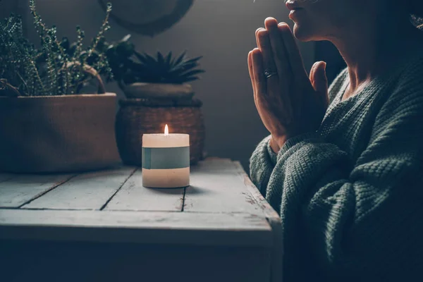 Concept of inner life balance and meditation with woman praying with clasped hands in front of a fire candle at home in the dark. People pray and meditate. Wellbeing in alternative lifestyle female
