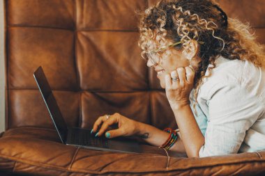İnternet üzerinde insan aktivitesi kavramını araştır. Kanepede yatan bilgisayarın önünde mutlu bir kadın gülümsüyor. Bir kadın, dizüstü bilgisayarını boş zaman ve iş için kullanıyor. Rahat bir şekilde kanepeye uzanıyor.