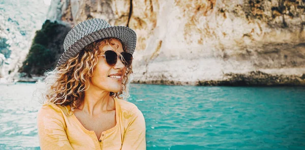 Outdoor portrait of an attractive tourist woman smiling and enjoying outdoor leisure activity with a blue lake or river in background. Happy female people with hair and sunglasses and trendy style