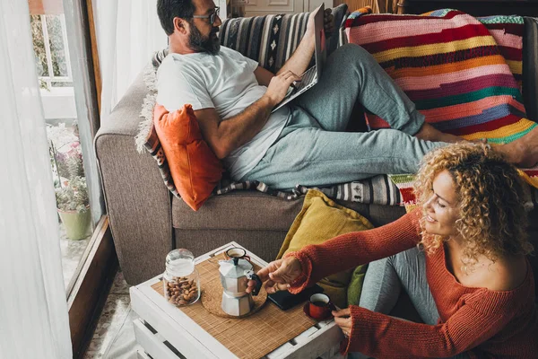 Couple in romantic leisure activity at home having breakfast together. Man using laptop and woman drinking coffee, smiling. Real life and people enjoying apartment. Sunday time and holiday