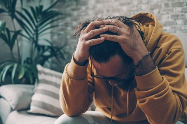 Man holding his head alone at home for desperation and stress emotions. Concept of tired adult and personal crisis. Sadness and stressed portrait of male indoor. Having problems and worried. Bad news