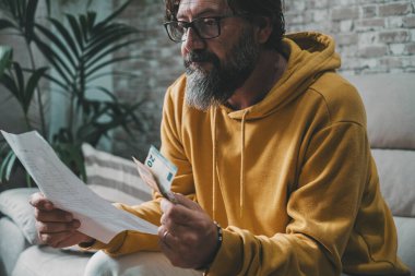 Man with economy problems looking bills and costs document and taking last banknotes on hand. Worried expression portrait. People looking for business job solution. Family and crisis concept life