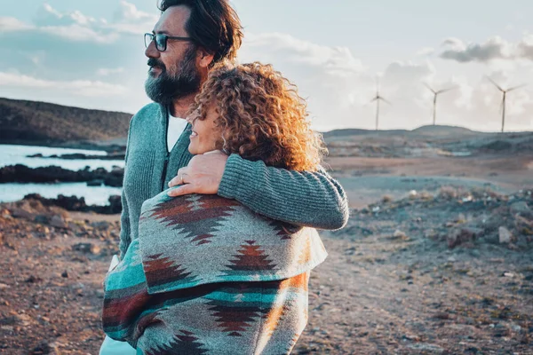 Romantic people, man and woman hugging and admiring beautiful landscape panorama together. Travel couple enjoying outdoor romance activity with wind turbines in background. Couple in love outdoor