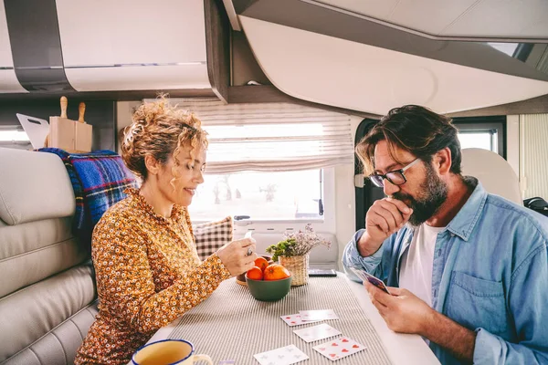 One middle age couple enjoy time playing cards together inside a travel home camper van. People enjoying time on vacation smiling and having fun. Man and woman in road trip summer holiday van life