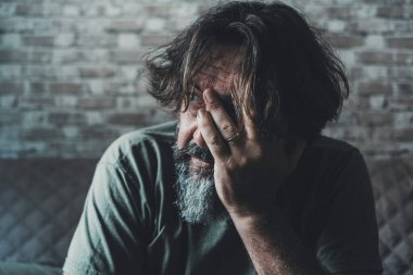 Desperate and stressed man touching his face with hand and looking outside at home. Problems and worried people indoor. End of relationship and love for husband sitting on toe sofa. Economy failure