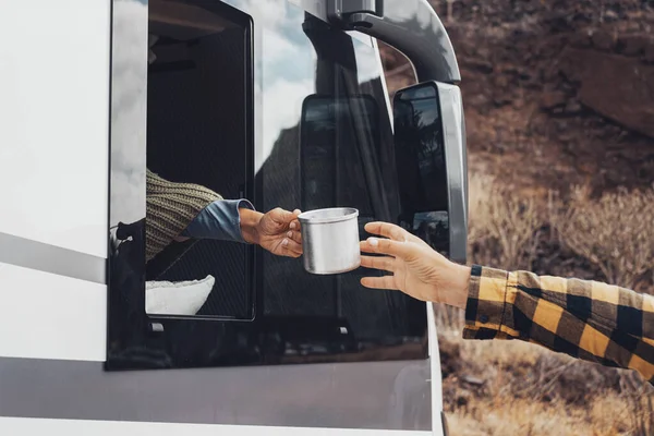 Concept of tourism and adventure with camper van vanlife lifestyle people. Woman giving cup of coffee to a man from the interior of motor home. People enjoying road trip holiday vacation camping car