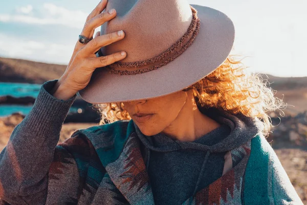 Close up of beauty portrait of woman hidden face under a traveler hat. Outdoor leisure activity female with trendy clothes. Concept of travel lifestyle people. Pretty lady model outdoor in sunset time