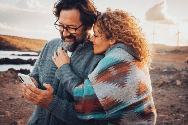 Romantic couple of traveler tourist use mobile phone together with love and relationship in outdoor leisure activity. Desert and countryside background with wind turbine windmills. Concept of travel