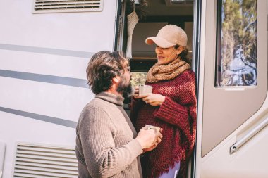 Couple of young mature people enjoy time talking outside the door of a modern camper van during summer holiday travel vacation. Man and woman together living on a motor home with nature outdoors