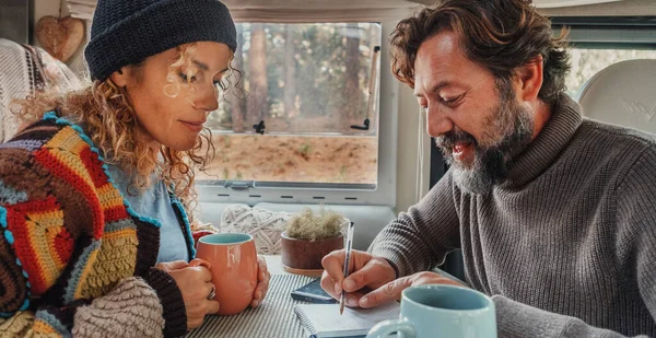 The couple plan travel destination from inside a camper van. Man and woman indoor leisure activity together in modern motor home interior. Concept of vanlife and living off grid for alternative people