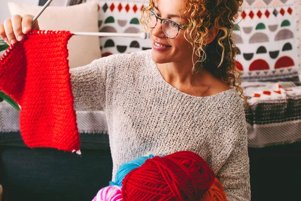 One happy woman at home look satisfied, a knit work with red wool. Female at home with hobby making warm clothes. Happy young people lady smile and enjoy leisure indoor. Hand made garment concept job