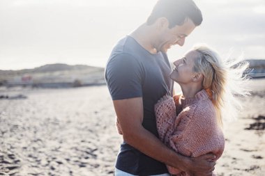 Dışarıda birbirini seven mutlu bir çift gülümsüyor ve birbirlerine sarılıyorlar. Yetişkin bir adam ve genç bir kız birlikte romantizm ve şefkatle gözlerinin içine bakıyorlar. Yaz balayı tatil yaşam tarzı