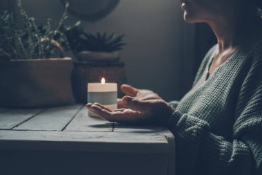 Zen meditasyonunda evde bir kadın ve arka planda mum ışığı. Elleri havada bir kadın, karanlık ışıkta tek başına dua edip meditasyon yapıyor. Sağlıklı zihinsel yaşam tarzı kavramı. Doğa