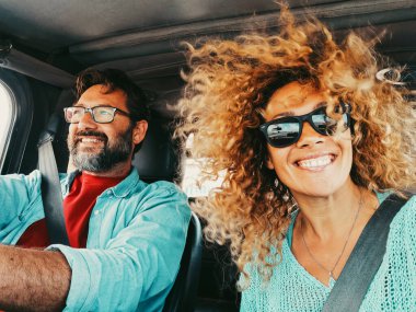 Arabayla seyahat eden mutlu genç çift eğleniyor. Araba sürerken kocasıyla fotoğraf çeken bir kadın. Ulaşım. Arabanın içinde emniyet kemeri olan insanlar eğleniyor.