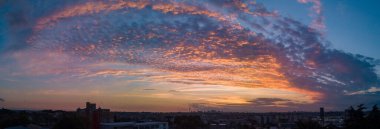 Günün sonunda bulutlar arasında bir gökyüzü ve çok renkli, mavi ve turuncu renklerle. Görüntünün temelinde ve arka planında şehrin silueti var..