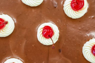 Çikolata kaplı yuvarlak pasta, üstünde kiraz ve krem şanti var..