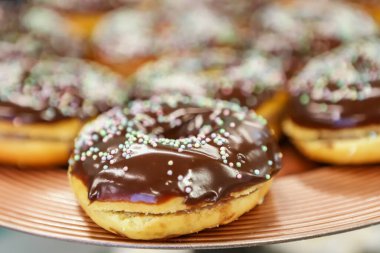 Kahverengi bir tabakta çikolatalı çörekler ve üstüne de küçük renkli şeker konfetileri.