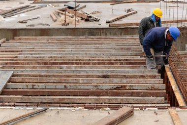 Sivil inşaat işçileri, yüzü tanımlamadan, gelecekte somutlaştırılacak bir parçanın yapısal demir çerçevesini taşıyorlar..