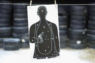 Atış talimlerinde kullanılan beyaz ve siyah renkli hedef, arka planda kurşun delikleri ve lastikler var.