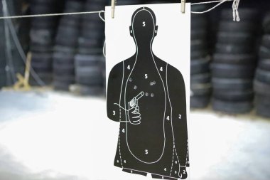 Atış talimlerinde kullanılan beyaz ve siyah renkli hedef, arka planda kurşun delikleri ve lastikler var.