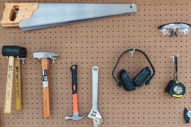 Duvarda testereler, gözlükler, mezura ve çekiç gibi çeşitli aletlerle asılı duran resim.