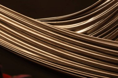 Birbirlerine bağlanmış altın kumaşlar siyah renkle çelişen dalgalanmalar oluşturuyor.