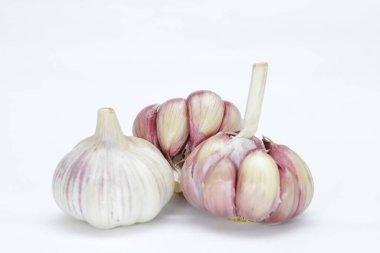 Üç baş sarımsak (Allium sativum), biri hala soyulmamış ve diğeri hafif soyulmuş, her karanfil kenarlarda ve nötr bir arka planda pembe tonlarda görülebilir.