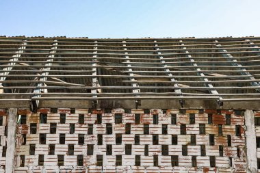 Duvarı kil renginde açık tuğlalarla kaplı ve zamanla solmuş beyaz bir boya var. Yukarısı içi boş tuğla ve çatının olduğu ve terk edildiği yer gibi görünüyor..