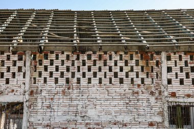 Duvarı kil renginde açık tuğlalarla kaplı ve zamanla solmuş beyaz bir boya var. Yukarısı içi boş tuğla ve çatının olduğu ve terk edildiği yer gibi görünüyor..