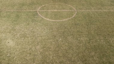 Orta çemberde yamuk çizgiler ve yıpranmış çimlerle bir futbol sahası görüntüsü..