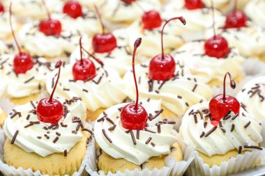Various mini cakes with whipped cream, chocolate sprinkles and cherries on top, as the focus on these.