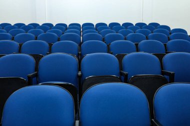 Rows of several blue chairs in an auditorium, or theater, with no person and all seats the same.