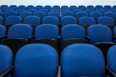 Rows of several blue chairs in an auditorium, or theater, with no person and all seats the same.