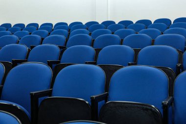 Rows of several blue chairs in an auditorium, or theater, with no person and all seats the same.