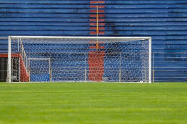 Yeşil çimenli bir futbol sahası, arka planda tribünler, insanlar olmadan, kırmızı ve maviye boyanmış..