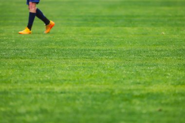 Bir futbol sahasının yeşil çimenleri, görüntünün ortasında seçici bir odak noktası, görüntünün üstünde kramponlu ayaklar..