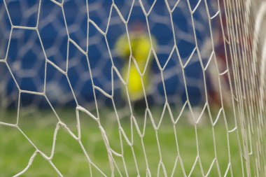 Ön planda futbol ağı, arka planda bulanıklık var, sarı takımlı bir oyuncunun siluetini görebilirsiniz, ve sahanın geri kalanı.