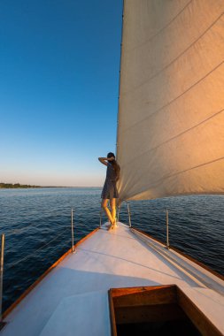 bir yatla seyahat etmek. Kız geminin pruvasında duruyor ve uzaklığa bakıyor. Beyaz bir yatın güvertesinde dinleniyor..