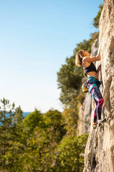 少女は岩に登る 登山列車は自然の地形を利用している 青い空を背景に困難な登山ルートを克服する女性 — ストック写真