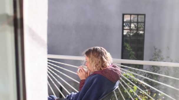 Dziewczyna siedzi z filiżanką na balkonie. — Wideo stockowe
