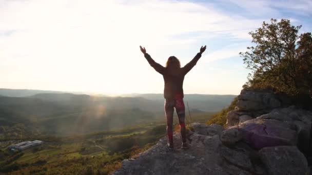 Gadis muda mengangkat tangannya ke matahari terhadap latar belakang pegunungan — Stok Video