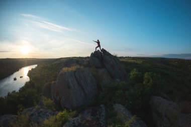 Uçurumun tepesinde bir kadın, dağın tepesinde bir kız silueti, güzel bir yerde gün batımı, resim gibi yerlere seyahat.