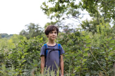 Sırt çantalı bir çocuk ormanda yürüyor, bir çocuk vahşi hayatı keşfediyor, bir çocuk ağaçların arasında tek başına duruyor, bir çocuğun portresi.