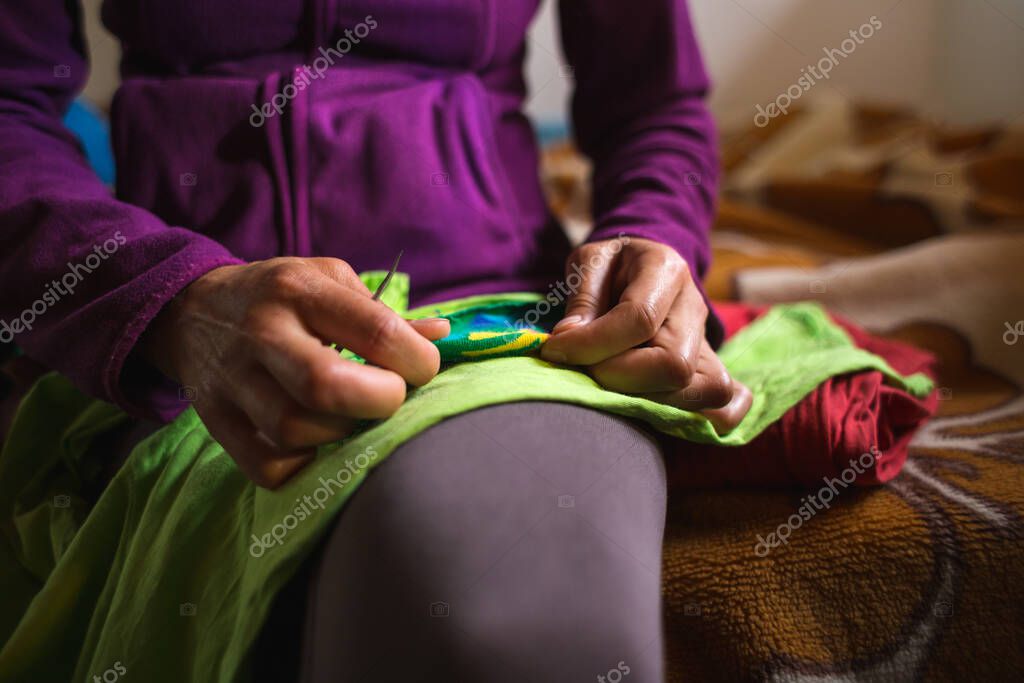 Una mujer cose un parche en la ropa rasgada de un calcetín viejo ...