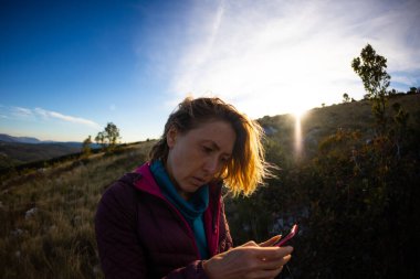 Bir kadın dağın tepesinde duruyor ve akıllı telefona bakıyor. Bir kız yol bulmak için navigatör kullanıyor.