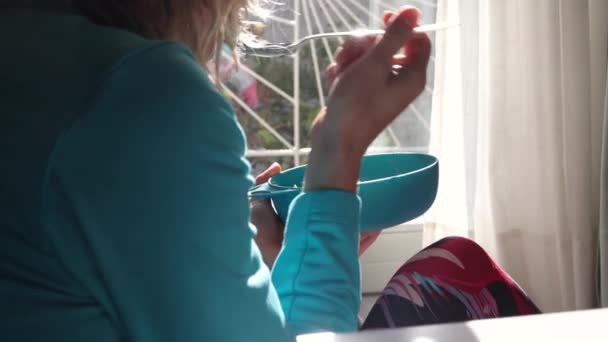 Gadis makan dari mangkuk dan memeriksa pesan di smartphone — Stok Video