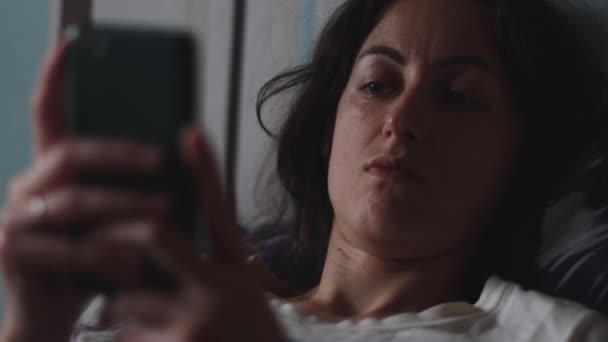 Het meisje zit op het bed en kijkt naar de smartphone — Stockvideo