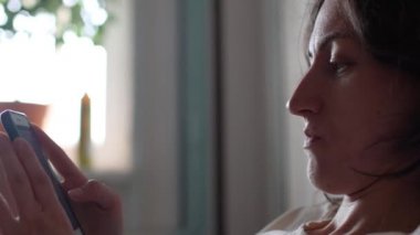 Kız yatağa oturur ve akıllı telefona bakar.